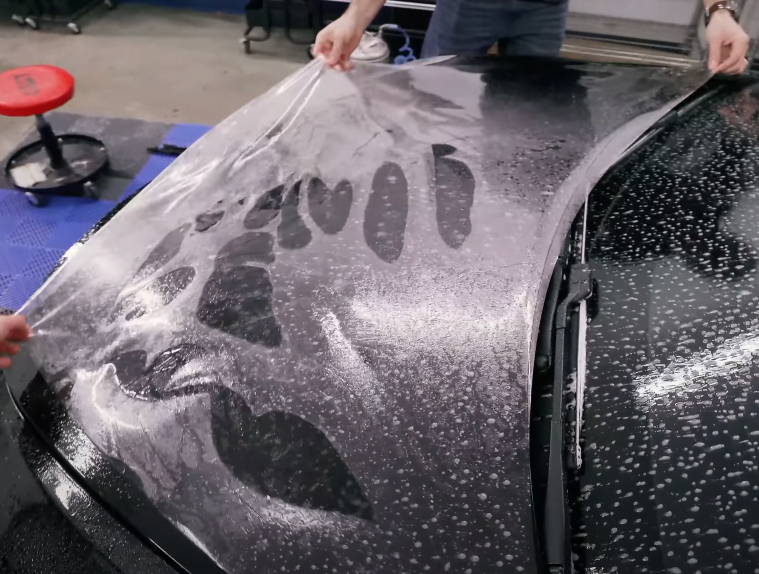 The installation of paint protection film (PPF) on the hood of a car.